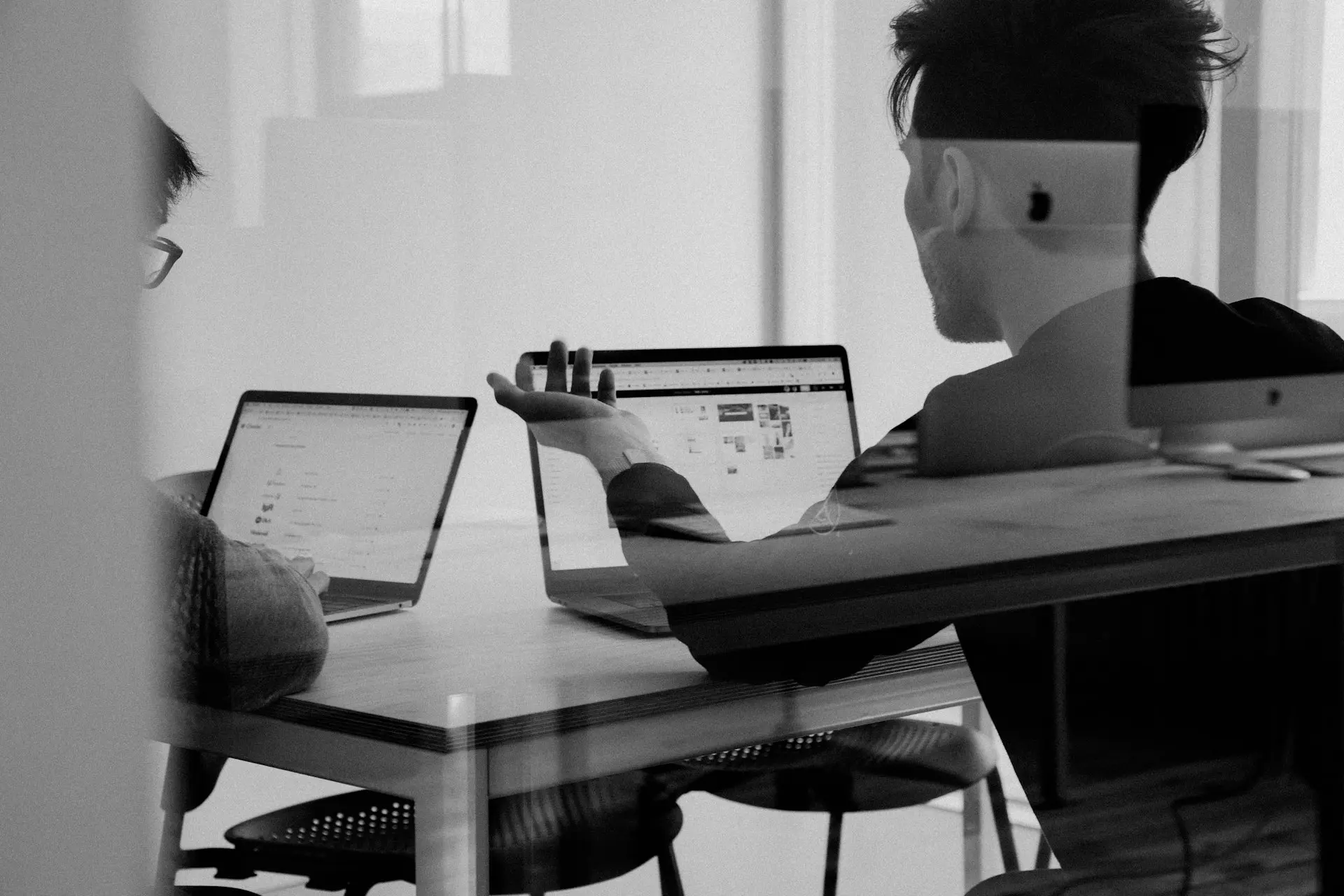 Zwei Personen an einem Tisch sitzend von hinten fotografiert. Beide benutzen ein MacBook